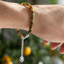 Load image into Gallery viewer, Bracelet with green and orange beads on a wrist against a blurred natural background
